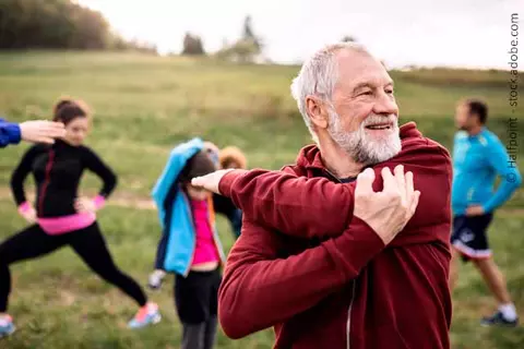 Mann mit Sportgruppe beim Dehnen im Freien